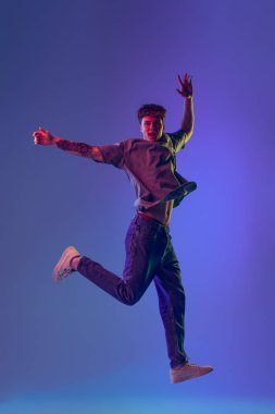Genç, kızıl saçlı bir adam, mavi stüdyo arkaplanının üzerinden neon ışıklarıyla atlayan bir öğrenci. Gençlik kavramı, moda, duygular, yüz ifadesi. İlan için alanı kopyala