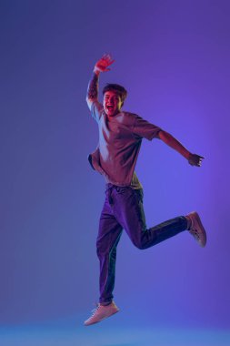 Genç, kızıl saçlı bir adam, mavi stüdyo arkaplanının üzerinden neon ışıklarıyla atlayan bir öğrenci. Gençlik kavramı, moda, duygular, yüz ifadesi. İlan için alanı kopyala