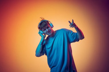 Duygusal, kızıl saçlı, kulaklıklı, sarı arka planda izole edilmiş müzik dinleyen genç bir adam. Gençlik kavramı, moda, duygular, yüz ifadesi. İlan için alanı kopyala