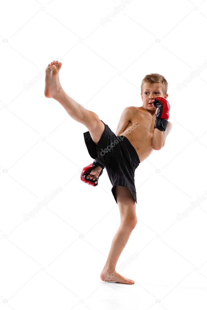 One little boy, sportive kid in black shots and gloves training thai boxing on white studio background. Beginner fighter of mma in action, motion, sport, education concept. Copy space for ad