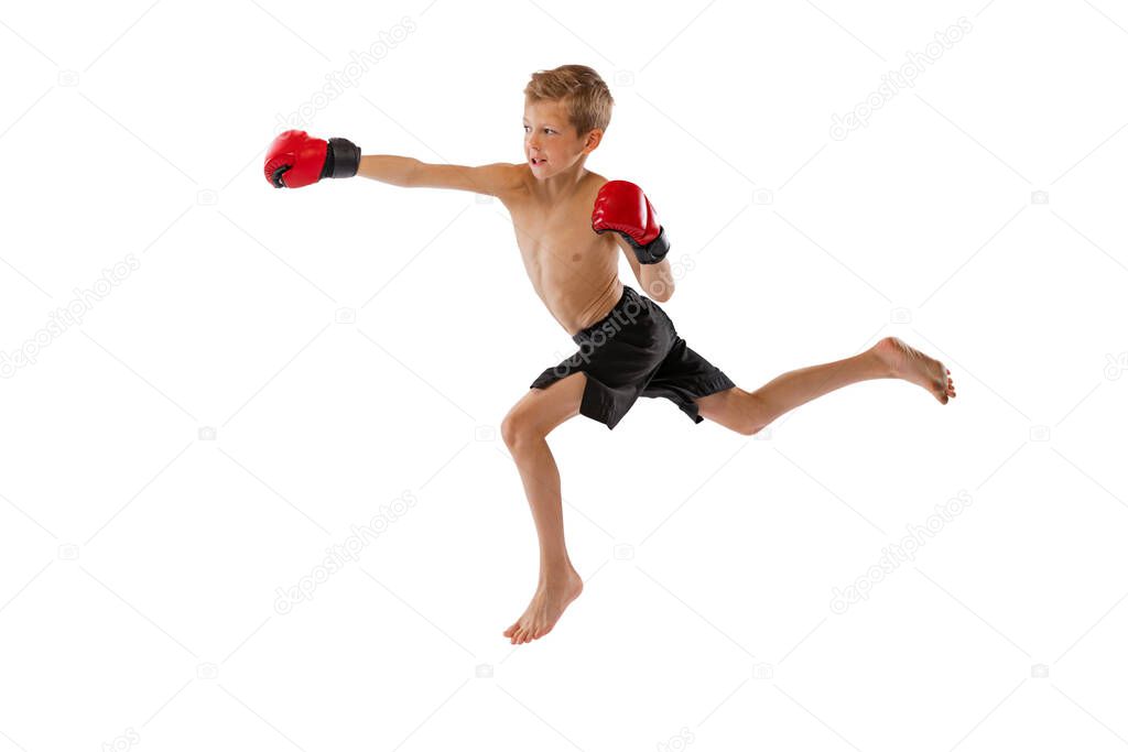 Punching. Little boy, kid in sports shots and gloves practicing thai boxing on white studio background. Beginner fighter of mma in action. Sport, challenges, action, motion concept. Copy space for ad