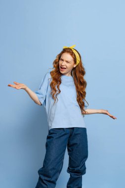 Sinirli genç kızıl saçlı kız, öğrenci mavi stüdyo arka planında izole edilmiş poz veriyor. İnsani duygular, yüz ifadesi kavramı. Moda renkleri. Gençlik kültürü, satış, indirim. İlan için alanı kopyala