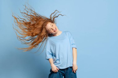 Eğlence, neşe. Duygusal genç kızıl saçlı kız, mavi stüdyo arka planında kafasını sallayan öğrenci. İnsani duygular, yüz ifadesi kavramı. Gençlik kültürü, satış, indirim. İlan için alanı kopyala