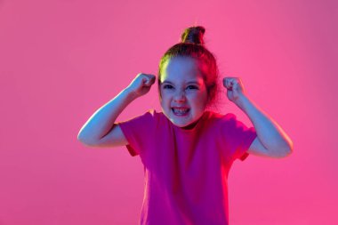 Kızgın görünüyor. Şirin küçük bir kızın portresi, pembe tişört giyen çocuk eflatun renkli arka planda yalnız poz veriyor. Çocuk duyguları, moda, güzellik, çocuk psikolojisi kavramı.