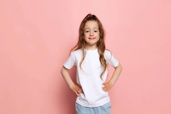 보이고 행복해 보이네 스튜디오에서는 귀여운 소녀가 분홍색 배경에 고립된 티셔츠를 — 스톡 사진