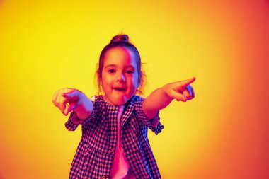 Vay canına, el kol hareketi. Duygusal sevimli küçük kız, sarı kırmızı arka planda izole edilmiş, neon ışıkta poz veren çocuk. Çocuk duyguları, moda, güzellik, okul ve reklam kavramı.