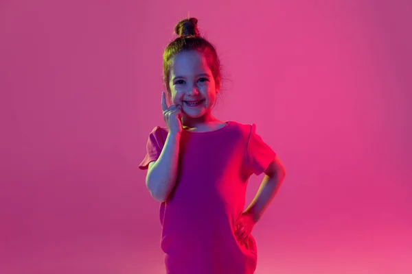 Ideas. Portrait of cute little girl, kid wearing pink t-shirt posing isolated on magenta color background. Concept of children emotions, fashion, beauty, school and ad concept.