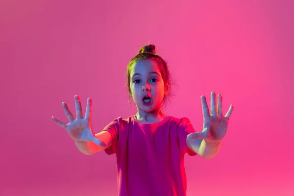 Stop sign, gesture. Portrait of cute little girl, kid wearing pink t-shirt posing isolated on magenta color background. Concept of children emotions, fashion, beauty, child psychology concept.