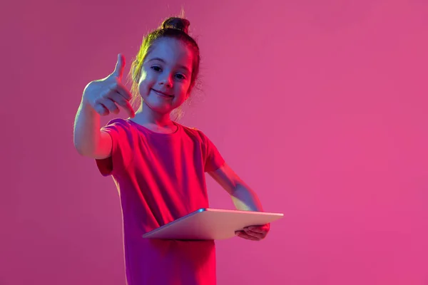 ガジェットを指してる 感情的な子供 就学前の年齢の女の子は マゼンタ色の背景に隔離されたデジタルタブレットでピンクのTシャツを着ています 子供の感情 ファッション 美しさ 教育概念の概念 — ストック写真