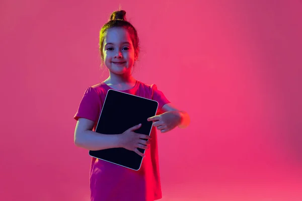 ガジェットを指してる 感情的な子供 就学前の年齢の女の子は マゼンタ色の背景に隔離されたデジタルタブレットでピンクのTシャツを着ています 子供の感情 ファッション 美しさ 教育概念の概念 — ストック写真