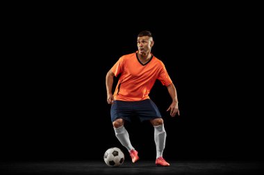 Top sürüyorum. Koyu arka planda izole edilmiş profesyonel erkek futbolcu portresi. Spor anlayışı, hedefler, rekabet, hobi, reklam. Turuncu-mavi futbol takımı giyen sporcular