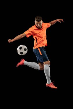 Bacak tekmesi. Koyu arka planda izole edilmiş profesyonel erkek futbolcu portresi. Spor anlayışı, hedefler, rekabet, hobi, reklam. Turuncu-mavi futbol takımı giyen sporcular