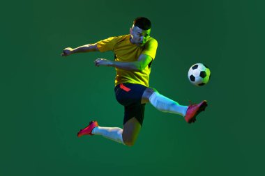 Dynamic portrait of professional male football soccer player in motion isolated on dark background. Concept of sport, goals, competition, hobby, ad. Sportsmen wearing orange-blue football kit clipart