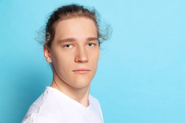 Açık görünüm. Mavi arka planda izole edilmiş genç bir öğrencinin yakın plan portresi. Duygusal, genç yüz. Erkek yarı boy portresi. İnsani duygular, yüz ifadesi kavramı. Moda renkleri