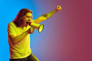 Haklar için savaş. Uzun kıvırcık saçlı, megafona bağıran heyecanlı genç adam mavi-pembe arka planda izole edilmiş. Güzellik, moda, gençlik kültürü ve duyguları kavramı. Erkek portresi.