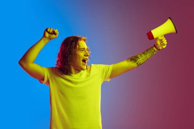 Haklar için savaş. Uzun kıvırcık saçlı, megafona bağıran heyecanlı genç adam mavi-pembe arka planda izole edilmiş. Güzellik, moda, gençlik kültürü ve duyguları kavramı. Erkek portresi.