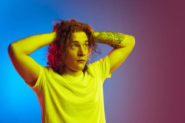 Şok oldum. Uzun kıvırcık saçlı, gradyan mavi-pembe arka planda izole edilmiş genç bir adam. Güzellik, moda, gençlik kültürü ve duyguları kavramı. Yarım boy erkek portresi. İlan için alanı kopyala