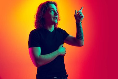 İşaret. Uzun kıvırcık saçlı, sarı kırmızı arka planda izole edilmiş genç, yakışıklı bir adam. Duygusal, genç yüz. Erkek yarı boy portresi. İnsani duygular, yüz ifadesi kavramı.