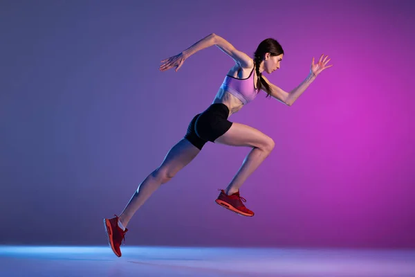 行动中 一个年轻的肌肉发达的女孩 女跑步者或慢跑者 在霓虹灯下被隔离在粉红蓝色的背景下 田径运动 竞赛和积极生活方式概念 — 图库照片