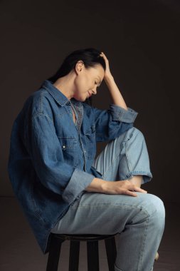 Düşünüyorum. Koyu arka planda yalnız poz veren mavi kot gömlekli 40 yaşında güzel bir kadın. Canlı portre, güzellik, moda kavramı. Uzun siyah saçlı bir model. İlan için alanı kopyala