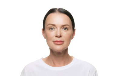 Kameraya bakıyorum. Beyaz arka planda iyi korunmuş orta yaşlı güzel bir kadının yarım boy portresi. Kozmetik, kaplıca, yaşla ilgili değişiklikler, yüz gerdirme ve cilt bakımı konsepti