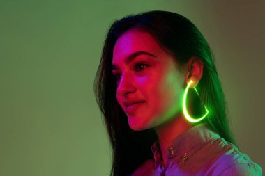 Küpeler. Moda neon aksesuarları olan genç ve güzel bir kız. Hafif arka planda izole edilmiş mücevherler. Güzellik kavramı, dijital moda tarzı, yaratıcılık, dijitalleştirme, teknoloji çağı, bilişim