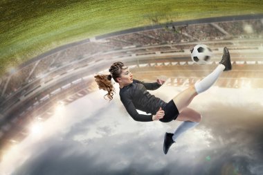 Young female soccer or football player with long hair in sportwear and boots kicking ball for the goal in jump at the stadium. Concept of healthy lifestyle, professional sport, hobby, motion, movement