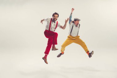 İki neşeli adam, eski moda kıyafetlerle koşan, atlayan, beyaz arka planda izole edilmiş eğlenen iki genç adam. Sanatçılar hareket halinde. Kültür kavramı, sanat, müzik, tarz, reklam