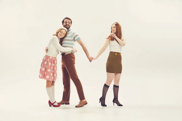 Love triangle, intrigue. One young man and two girl in vintage retro style outfits psoing isolated on white background. Concept of relations, family, 1960s american fashion style and art.