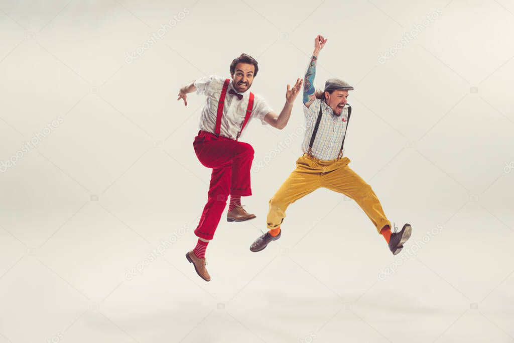 Two cheerfull dudes, young men in old-school fashioned attire running, jumping, having fun isolated on white background. Artists in motion. Concept of culture, art, music, style, ad