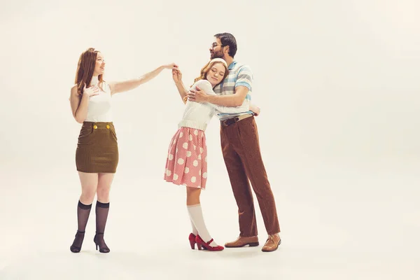 Love triangle, intrigue. One young man and two girl in vintage retro style outfits psoing isolated on white background. Concept of relations, family, 1960s american fashion style and art.