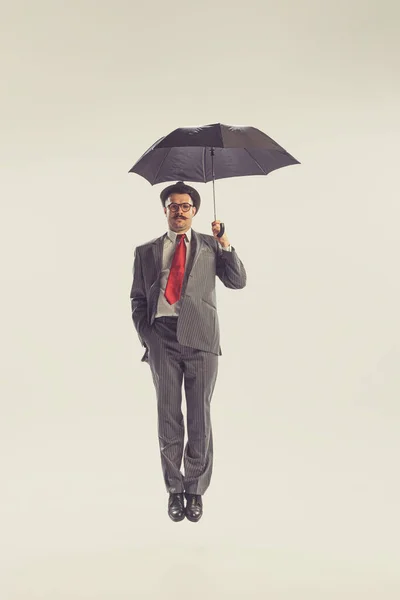 Bad weather. Portrait of young man dressed in 50s, 60s style fights the wind with umbrella isolated on white background. Autumn fashion collection. Concept of culture, art, wellbeing, beauty and ad.