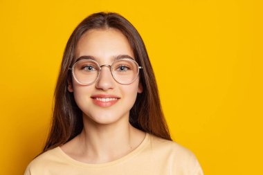 Sakin görünüyor. Sarı arka planda izole bir şekilde poz veren günlük kıyafetli duygusal çekici bir kız. Güzellik, sanat, moda, gençlik, satış ve reklamlar. Uzun siyah saçlı bir manken..