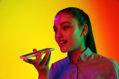 Neon ışıklarıyla izole edilmiş sarı arkaplanda izole edilmiş telefonu kullanan gülümseyen genç kızın yakın plan portresi. Duygular, yüz ifadesi, gençlik, arzu kavramı. İlan için alanı kopyala