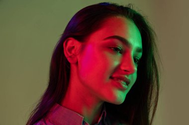 Hafif bir gülümseme. Gri arka planda, neon ışıkta izole edilmiş uzun siyah saçlı güzel bir kızın yarım boy portresi. Güzellik, sanat, moda, gençlik, satış ve reklamlar kavramı.