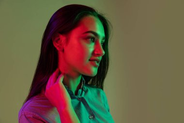 Cazibe. Gri arka planda, neon ışıkta izole edilmiş uzun siyah saçlı güzel bir kızın yarım boy portresi. Güzellik, sanat, moda, gençlik, satış ve reklamlar kavramı.