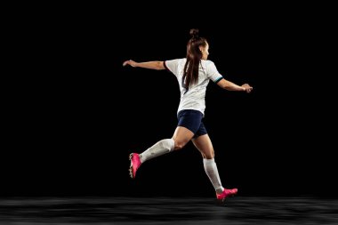Enerjik futbolun arka planı, koyu arka planda tek başına koşan futbolcu. Spor, aksiyon, yarışmalar, oyunlar ve fitness konsepti. Futbol takımı giyen genç sporcu..