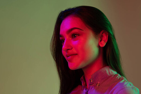 Beauty and grace. Half-length portrait of young pretty girl with long dark hair posing isolated on grey background in neon light. Concept of beauty, art, fashion, youth, sales and ads.