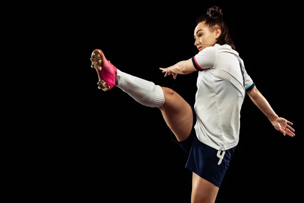 Young caucasian sportive woman, female soccer, football player in motion isolated on dark background. Sport, action, competitions, games and fitness concept. Young sportive wearing football kit.