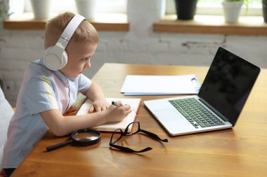 Uzaktan öğrenme. Sevimli küçük bir çocuk, okul çağındaki bir çocuk online ders dinliyor, evde dizüstü bilgisayar kullanıyor. Çevrimiçi eğitim, çocukluk, insanlar, ödev ve okul konsepti. Mutlu görünüyor, sakin.