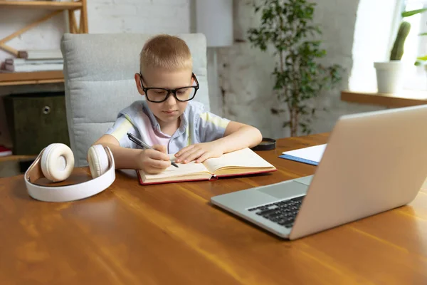 Remote learning. One cute little boy, school age kid listening online lesson, using laptop at home interior. On-line education, childhood, people, homework and school concept. Looks happy, calm