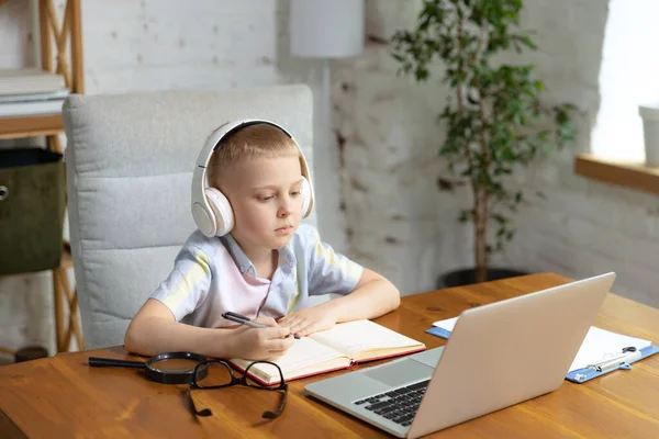 Remote learning. One cute little boy, school age kid listening online lesson, using laptop at home interior. On-line education, childhood, people, homework and school concept. Looks happy, calm