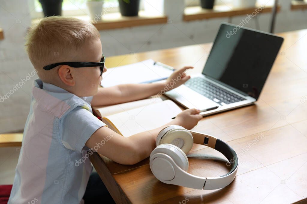 Using laptop. Happy school age kid sitting at home and doing homework at home interior, indoors. Online education, childhood, people, remote learning and school concept. Looks cheerful, delighted