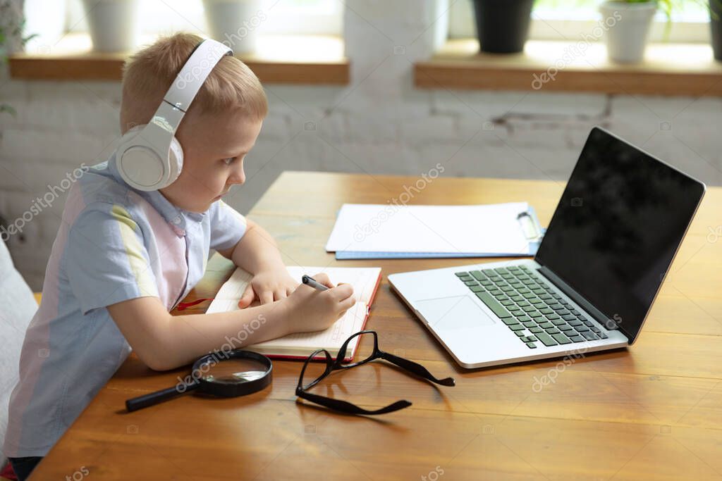Remote learning. One cute little boy, school age kid listening online lesson, using laptop at home interior. On-line education, childhood, people, homework and school concept. Looks happy, calm