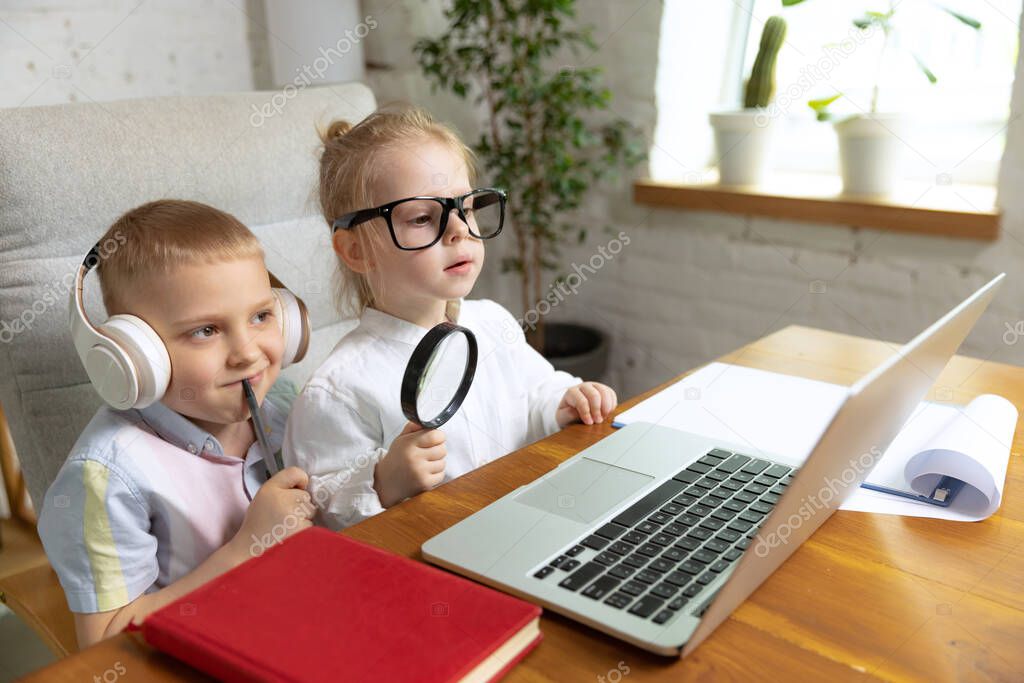 Happy kids, brother and sister sitting at home and doing homework at home interior, indoors. Online education, childhood, people, remote learning and school concept. Look cheerful, delighted
