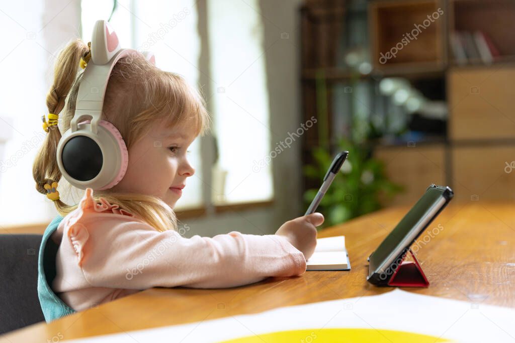 Online class in daycare. Live portrait of cute little girl, preschool age kid leaning at home using digital tablet. On-line education, childhood, people, homework and school concept. Looks happy, calm