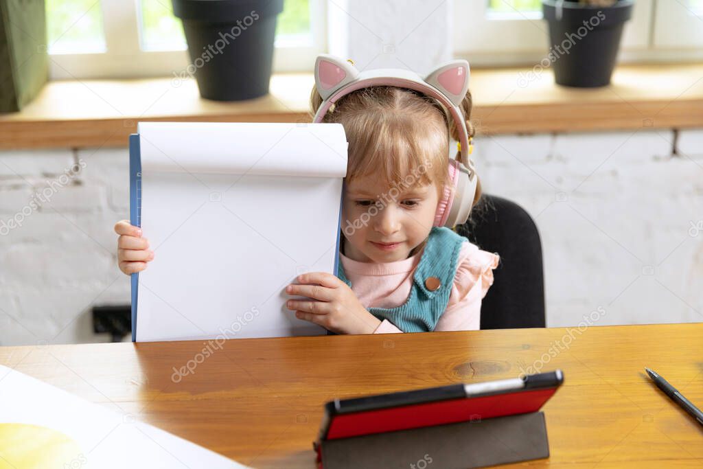 Showing drawing album. Live portrait of cute little girl, preschool age kid leaning at home using digital tablet. On-line education, childhood, people, homework and school concept. Looks happy, calm