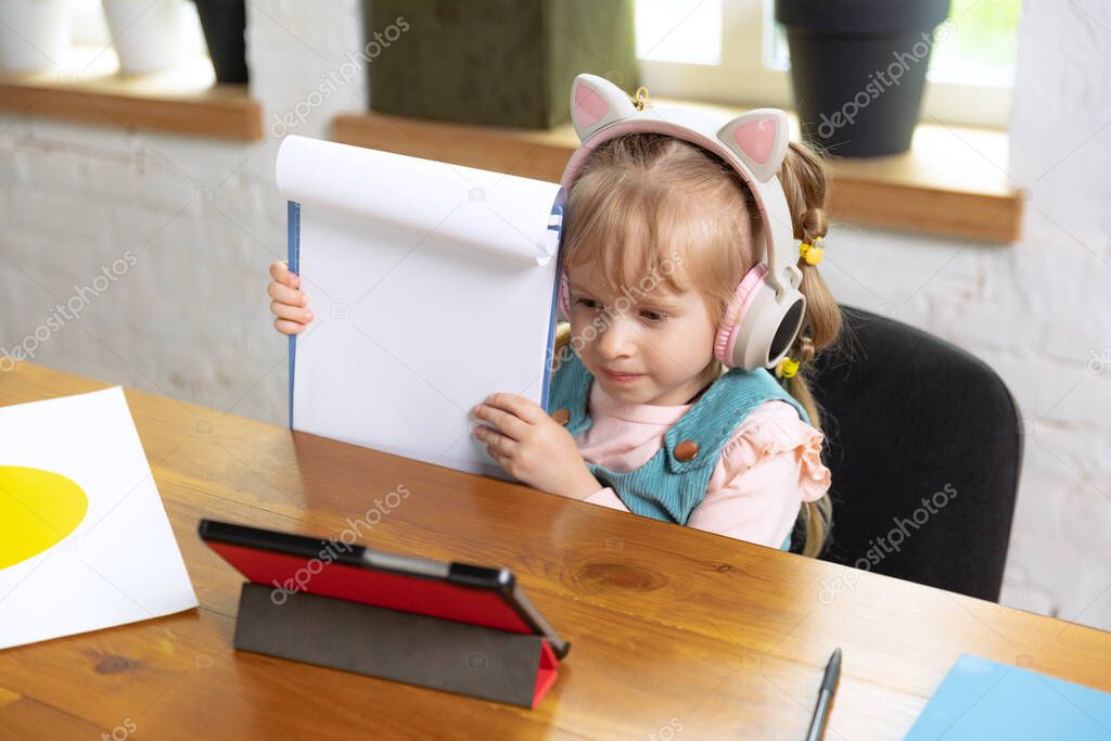 Showing her notebook. Live portrait of cute little girl, preschool age kid leaning at home using digital tablet. On-line education, childhood, people, homework and school concept. Looks happy, calm