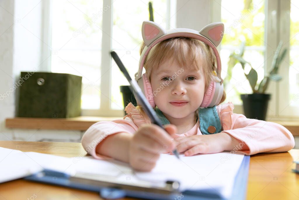 Write down. Live portrait of cute little girl, preschool age kid leaning at home using digital tablet. On-line education, childhood, people, homework and school concept. Looks happy, calm