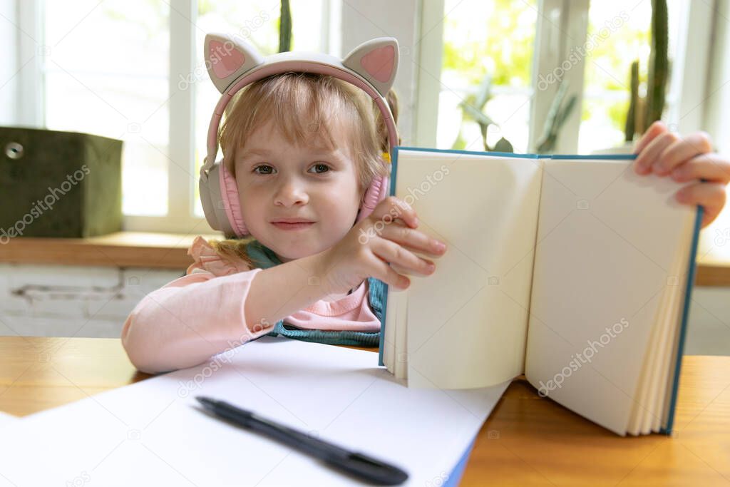 Looking at camera. Live portrait of cute little girl, preschool age kid leaning at home using digital tablet. On-line education, childhood, people, homework and school concept. Looks happy, calm
